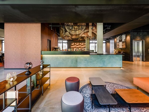 A spacious lobby with a central bar area, seating arrangements, and a high ceiling with industrial lighting. - Ibis Styles Friedrichshafen (Friedrichshafen)