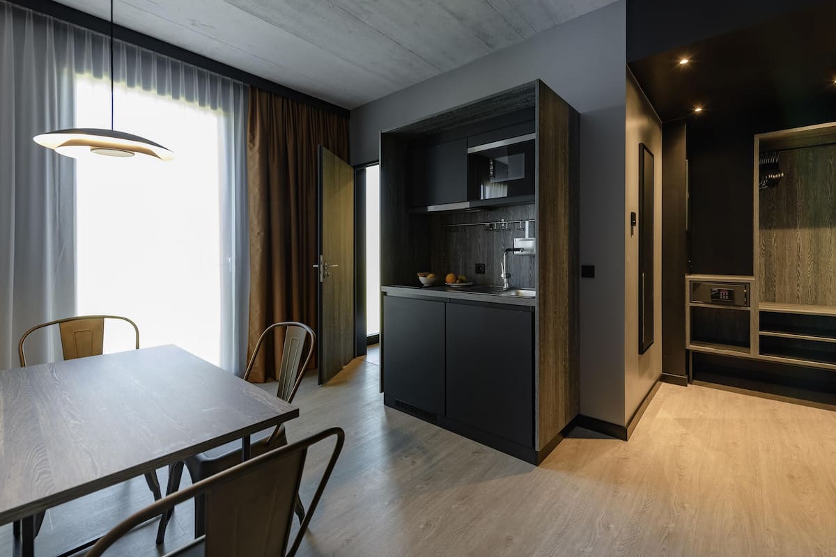 Une cuisine moderne avec des meubles de couleur sombre, un four encastré et un coin repas comprenant une table et des chaises en bois.