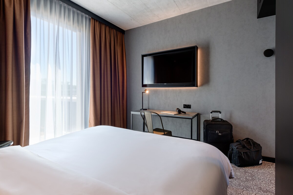 Une chambre d’hôtel avec un lit, un bureau équipé d’un ordinateur, un téléviseur fixé au mur et une valise posée sur le sol.