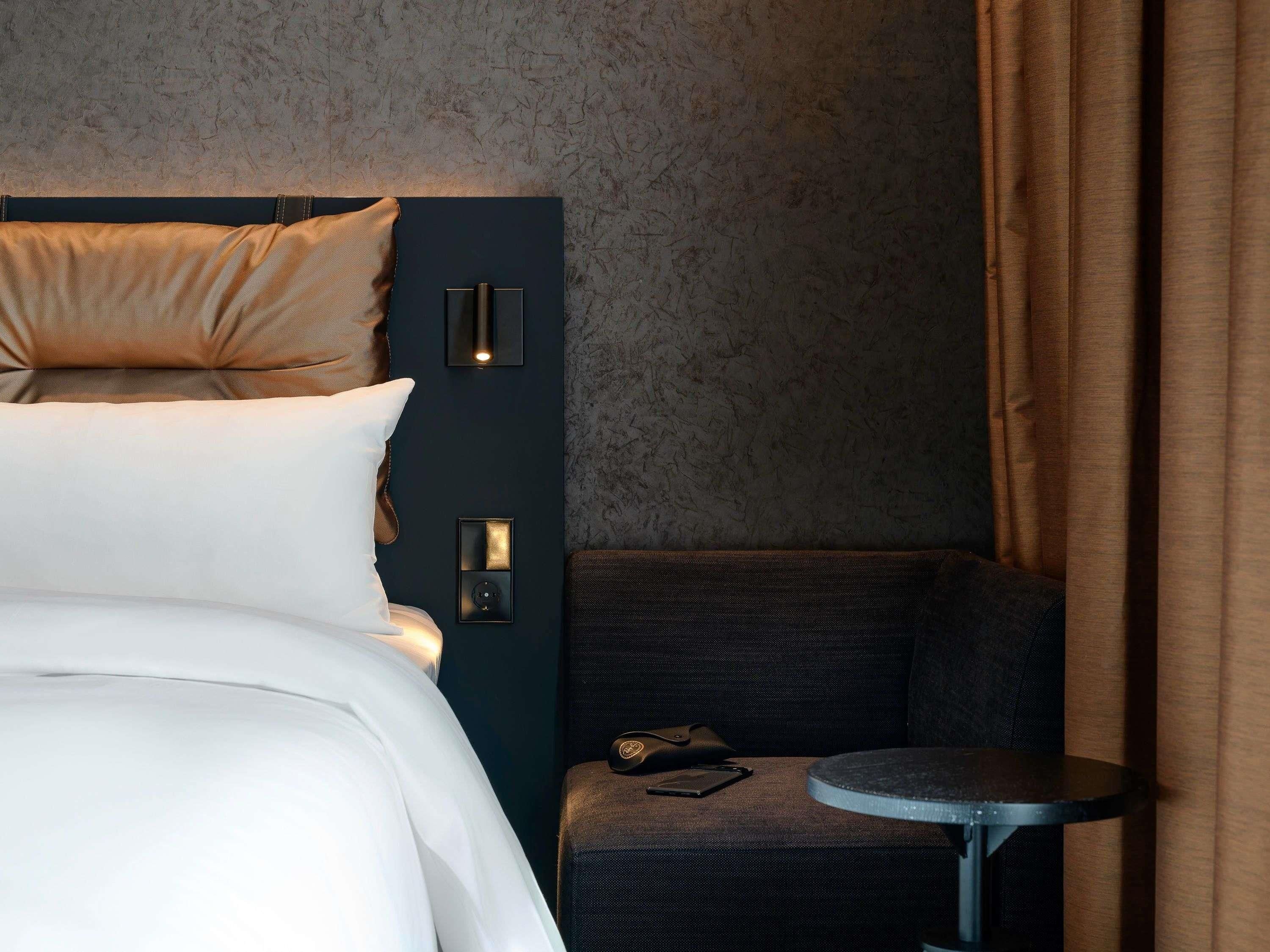 Een hotelkamer met een bed, een stoel, een klein rond tafeltje en wandlampen.