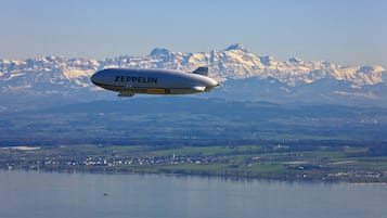 A Zeppelin airship flying over a lake with a mountainous landscape in the background.
