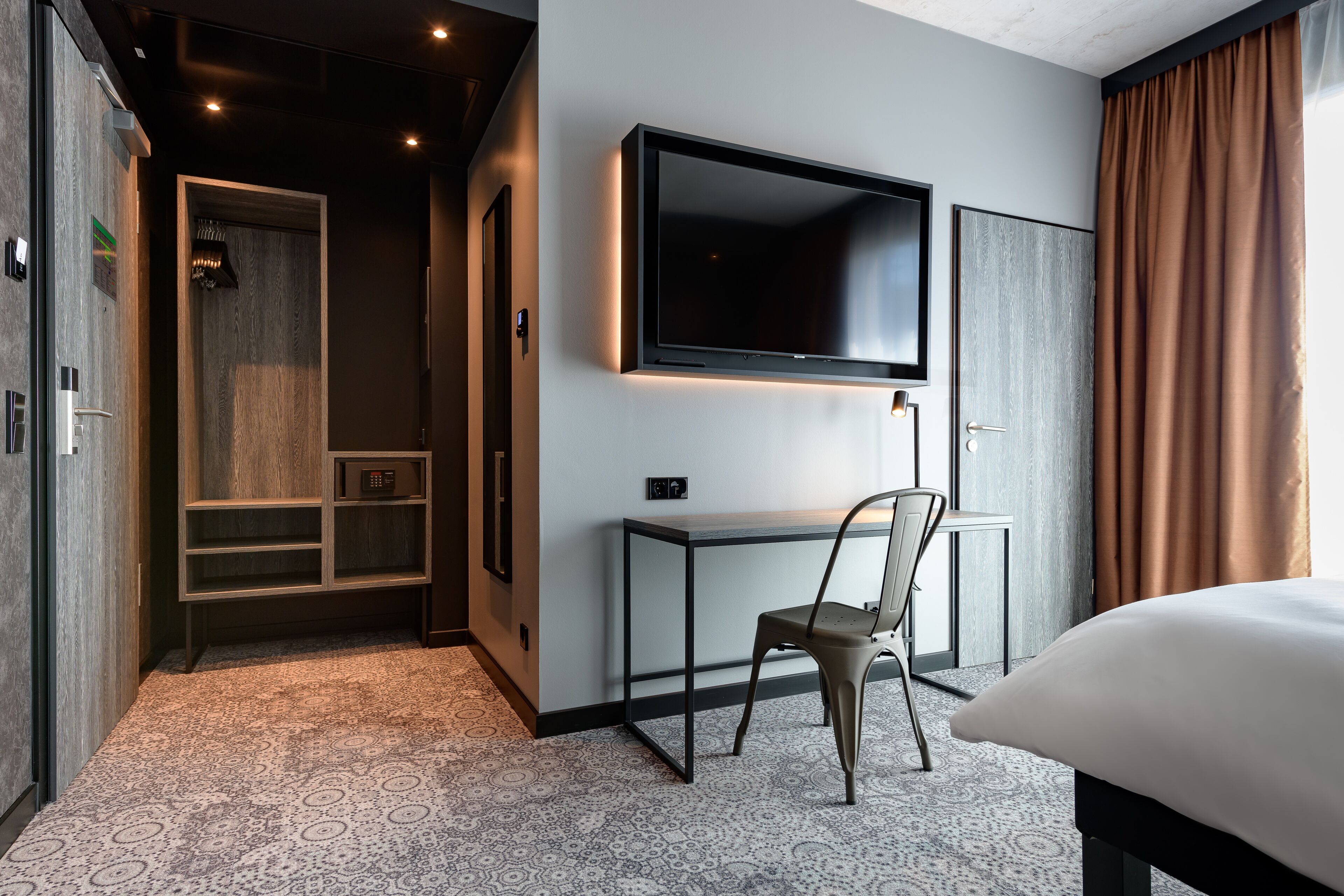 Habitación de hotel con cama, escritorio, silla, televisor y zona de ducha.