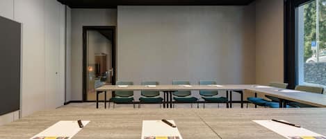 A conference room with a long table, multiple chairs, and a view through a large window.