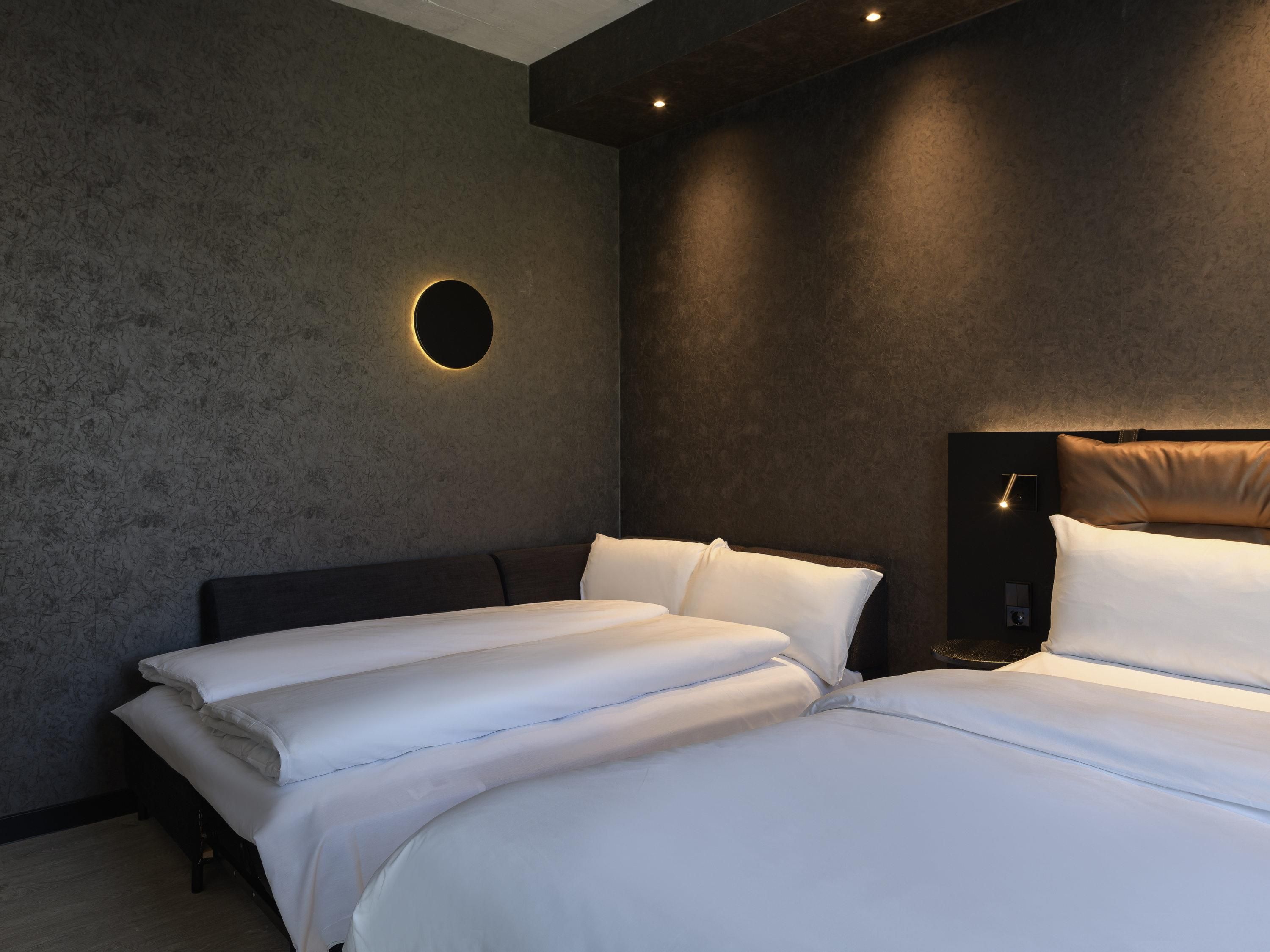 Een hotelkamer met twee bedden, een ronde wandlamp en een donker hoofdeinde.