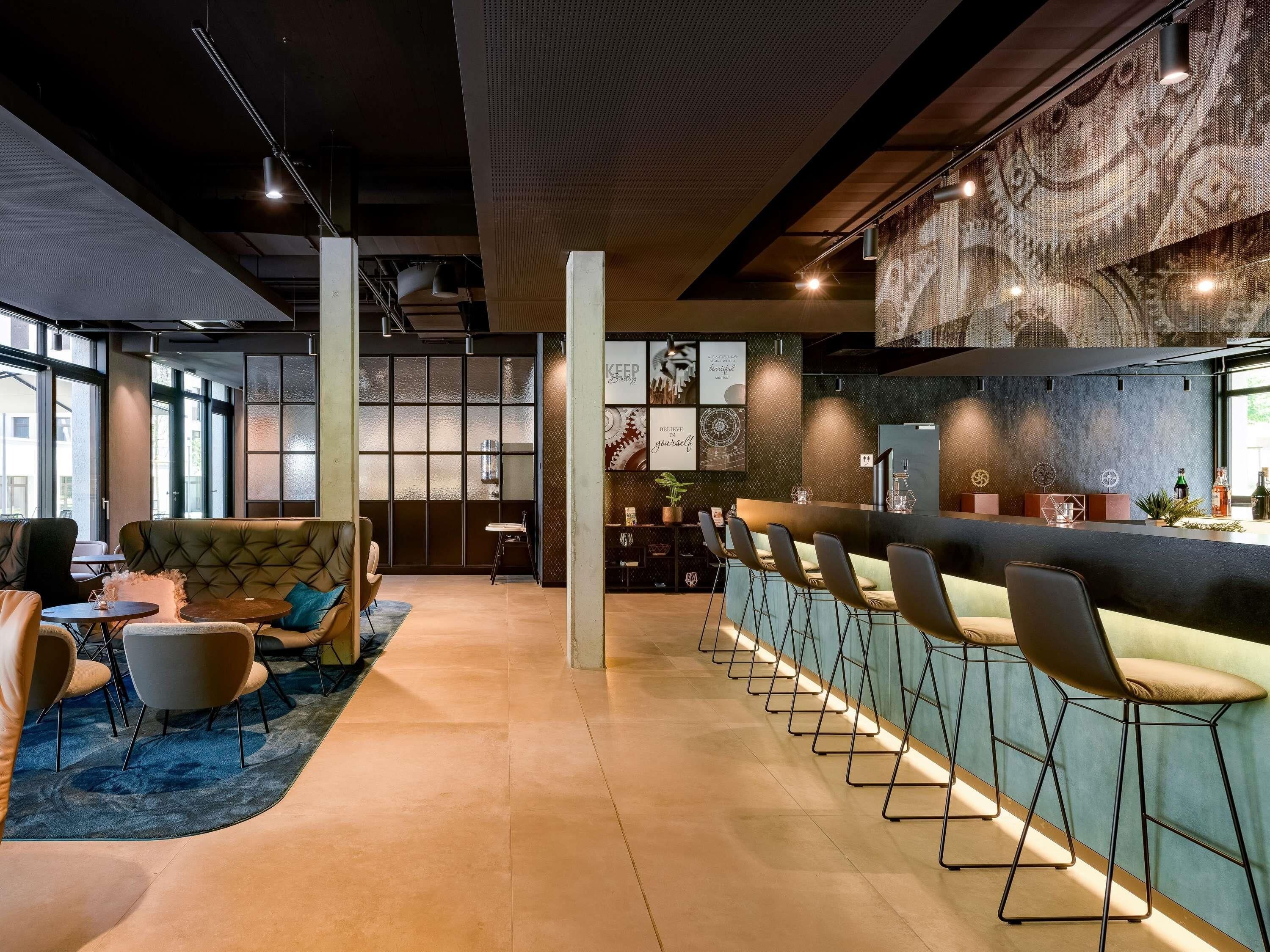 Un espace bar moderne doté d’un long comptoir, de tabourets et d’un coin salon avec un canapé et des fauteuils.