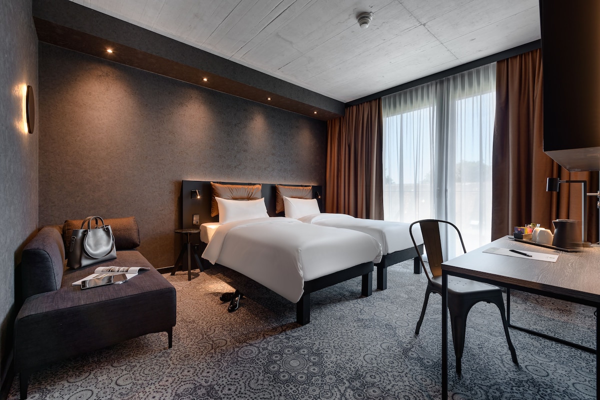 Une chambre d’hôtel avec un grand lit, un bureau, une chaise, un canapé et une fenêtre avec des rideaux.