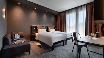 Habitación de hotel con una cama grande, un escritorio, una silla, un sofá y una ventana con cortinas.