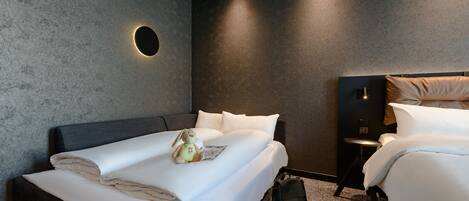 A modern hotel room with a large bed, a smaller bed, a round wall light, a small table, and a suitcase.