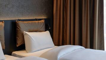 Habitación de hotel con dos camas, cabecero y ventana con cortinas.