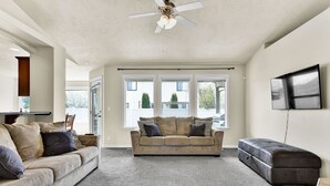 A spacious living room with a beige sofa, a dark leather ottoman, and a ceiling fan. - Spacious Cozy Home by Settlers Park --  Meridian, ID (Meridian)
