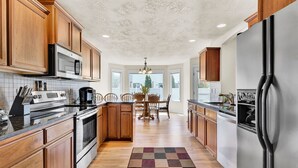 A kitchen with wooden cabinets, stainless steel appliances, and a central island with chairs. - Spacious Cozy Home by Settlers Park --  Meridian, ID (Meridian)