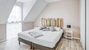 Een moderne slaapkamer met een schuine plafond, een bed met witte lakens, een houten hoofdbord en een nachtkastje met een lamp.