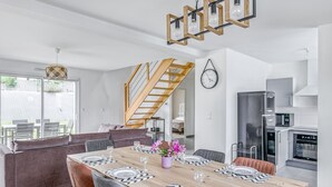 Een moderne keuken met roestvrijstalen apparatuur, een houten trap en een eethoek met een grote tafel gedekt voor vier personen.
