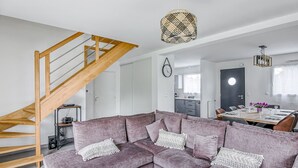 Een moderne woonkamer met een houten trap, een hoekbank, een eettafel en een keuken op de achtergrond.