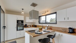 A modern kitchen with white cabinets, a wooden countertop, a built-in oven, and a large window. - La Roskoker - Villa 4 chambres et piscine privée proche plage - Roscoff (Roscoff)
