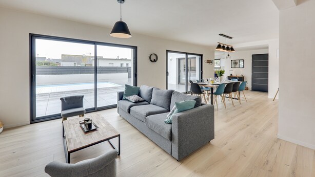 A modern living room with a grey sofa, a coffee table, and a dining area with a table and chairs. - La Roskoker - Villa 4 chambres et piscine privée proche plage - Roscoff (Roscoff)