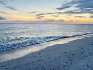 A beach with waves gently lapping onto the shore, a clear sky, and a distant horizon.