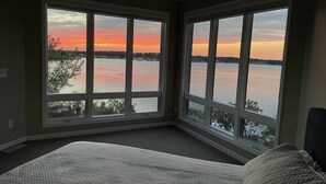 Un dormitorio con un amplio ventanal con vistas a un cuerpo de agua durante el atardecer.