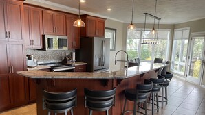 Una cocina moderna con armarios de madera oscura, una isla grande con taburetes de bar, electrodomésticos de acero inoxidable e iluminación colgante.