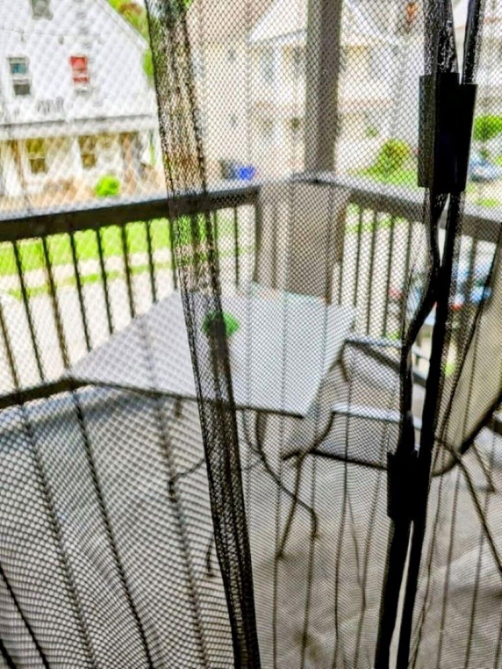 A balcony with a table and chairs, a railing, and a view of a house in the background.