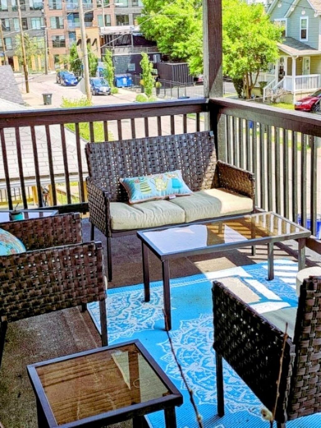 Een balkon met rieten meubels, een glazen tafel en een kamerkleed met patroon.