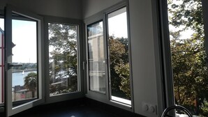 A room with three large windows, a view of a body of water, and a cityscape. - UNIQUE VIEW TOUR DE LA LANTERNE Apartment WITH TERRACE 2-4 PERS. (La Rochelle)
