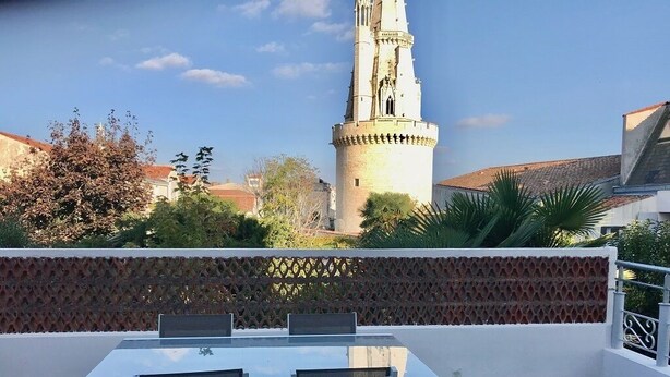 A terrace with a table and chairs, a decorative fence, and a tower in the background. - UNIQUE VIEW TOUR DE LA LANTERNE Apartment WITH TERRACE 2-4 PERS. (La Rochelle)