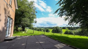 Een geplaveid terras met uitzicht op glooiende heuvels en een grote boom aan de rechterkant.