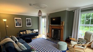 Een woonkamer met een blauwe bank, een open haard, een televisie en een groot raam met gordijnen.