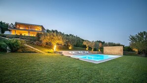 Uma casa moderna com piscina, cercada por gramado bem cuidado e árvores.