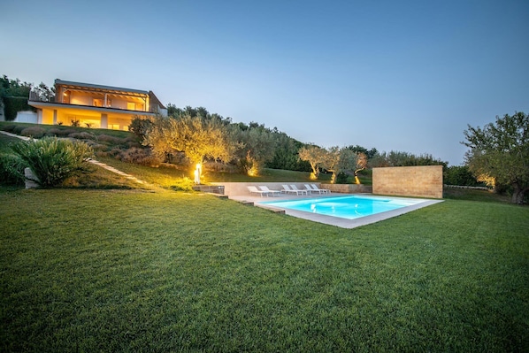 A modern house with a swimming pool, surrounded by well-maintained grass and trees.