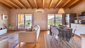 Ampla sala de estar com teto de madeira, um sofá, uma mesa de jantar posta para quatro pessoas e uma cozinha equipada com eletrodomésticos modernos.