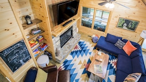 En mysig stuga med en inredning som inkluderar en öppen spis i sten, en blå soffa och en tv som är monterad på väggen.