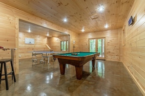 Een kamer met houten lambrisering, een pooltafel, een pingpongtafel en een biljarttafel.