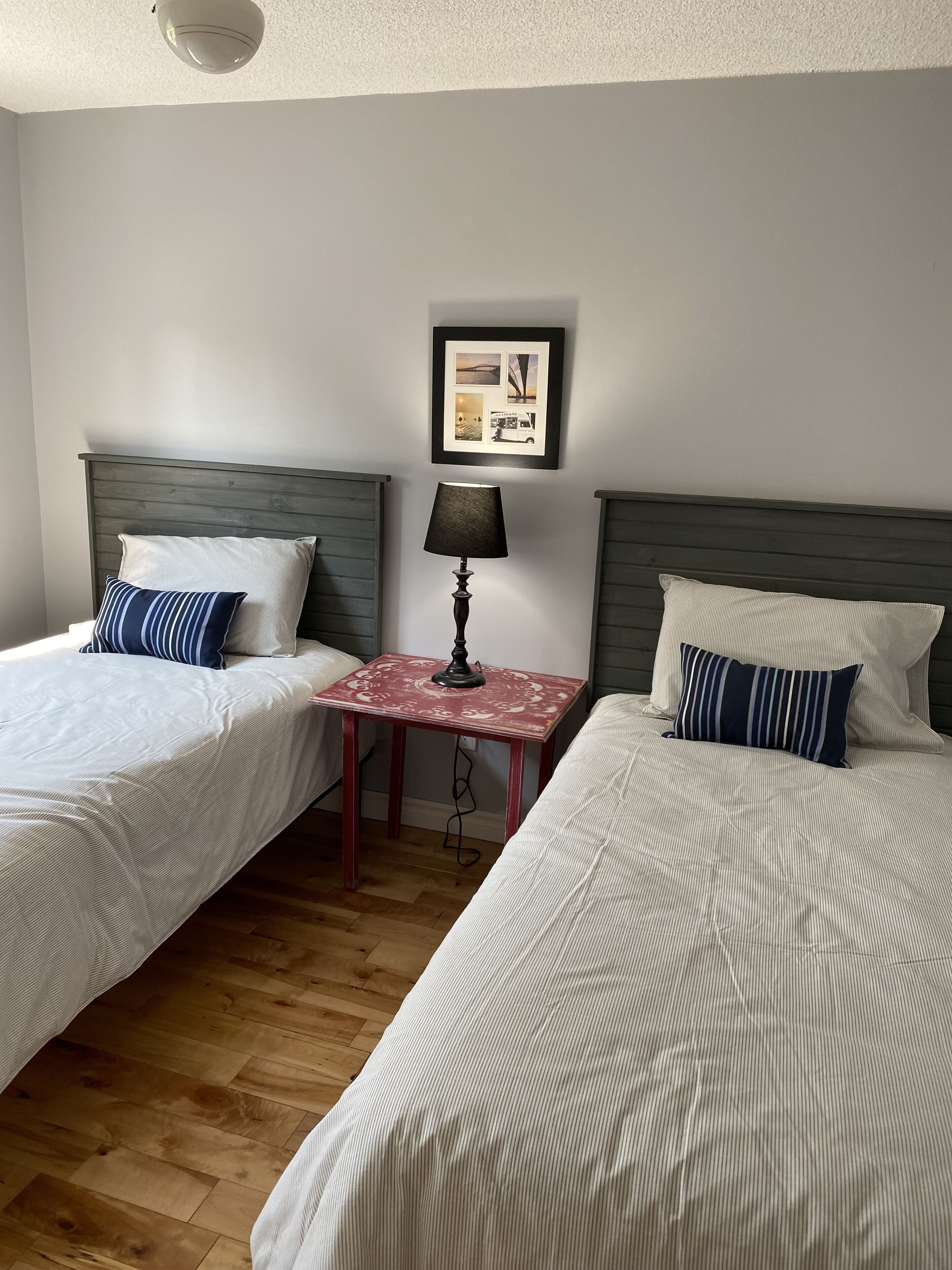 Una habitación con dos camas, una mesita con lámpara y un cuadro en la pared.