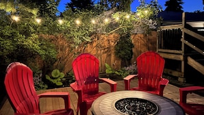 Un terrazzo con sedie rosse e un tavolo circolare, circondato da una recinzione in legno e luci decorative.