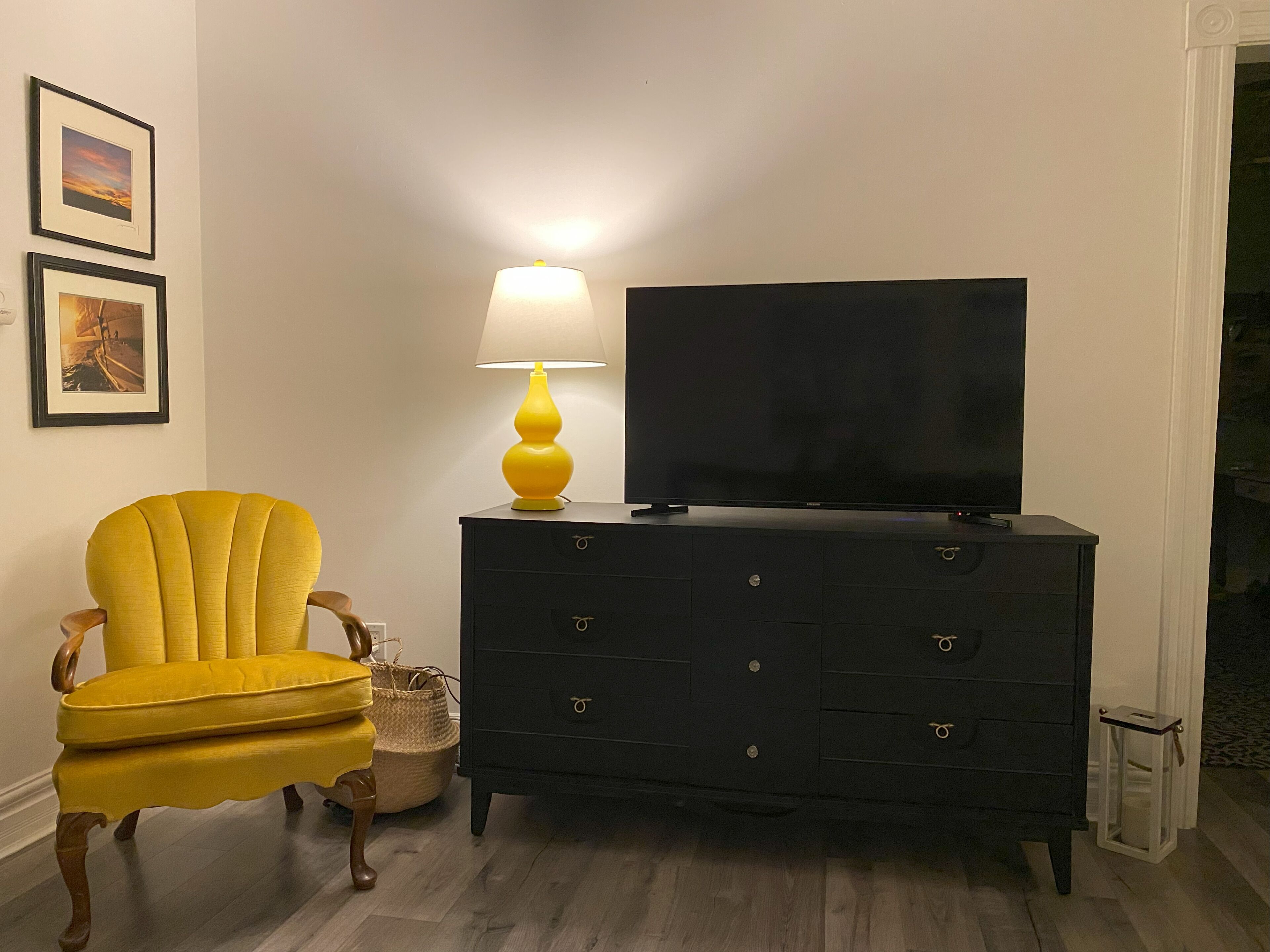 A room with a black dresser, a yellow armchair, and a television on top.