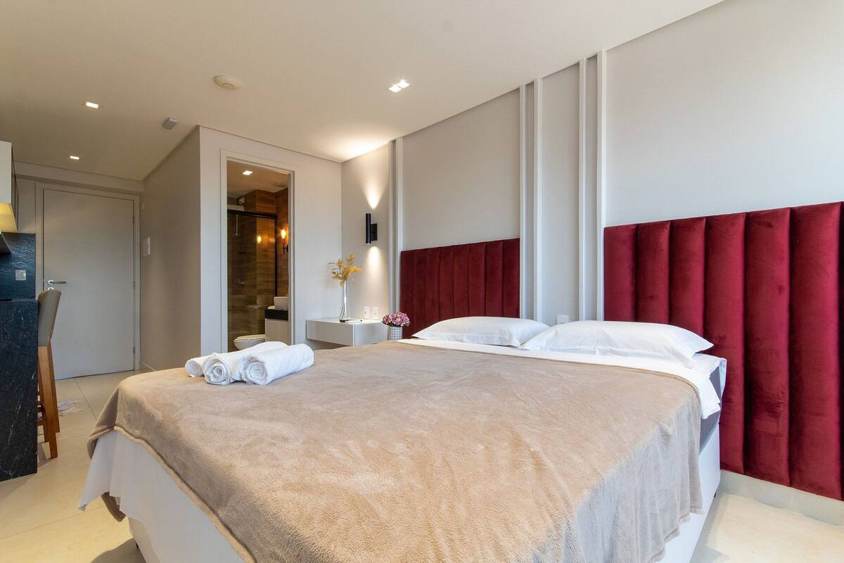 A modern hotel room with a large bed, a bedside table, and a bathroom visible through an open door.