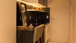 A compact kitchen with a black countertop, a white chair, and a small sink. - Incrível Suíte no Manaíra Apart Hotel (João Pessoa)