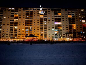 Ein mehrstöckiges Hotel mit Balkonen, ein Strand im Vordergrund und ein Neonzeichen darüber.