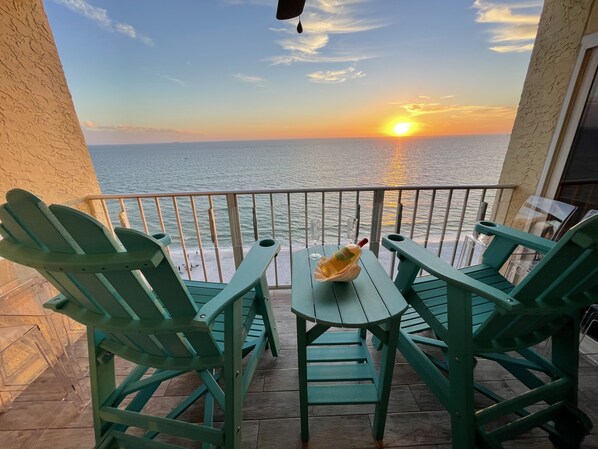 Un balcone con sedie verdi e un tavolo, con vista su un tramonto sul mare.