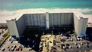 Eine Vogelperspektive eines großen Hotels mit einem zentralen Turm, einem Parkplatz und einem Strand im Hintergrund.