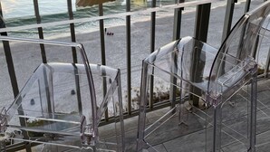 Ein Balkon mit transparenten Glastischen, einer Flasche Buckeye Winery Wein und einem Glas auf einer Brüstung mit Blick auf den Sonnenuntergang über dem Meer.