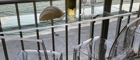 En balkon med glasstole, en flaske Buckeye Winery vin og et glas på gelænderet med udsigt til havet i solnedgang.