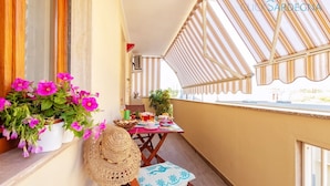 A balcony with a table set for tea, potted plants, and a straw hat.