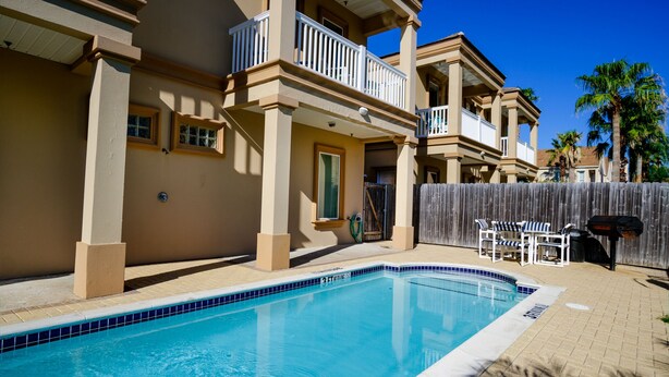 A residential building with a swimming pool, balconies, and a wooden fence. - Lovely 2-bedroom unit with a pool & workspace (South Padre Island)