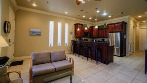 A spacious kitchen with dark wooden cabinets, a stainless steel refrigerator, and a bar area. - Lovely 2-bedroom unit with a pool & workspace (South Padre Island)