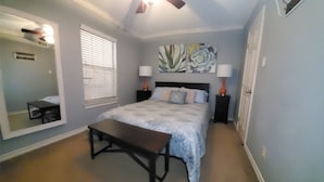 Une chambre à coucher comprenant un lit, des tables de chevet, un banc, un ventilateur de plafond et un grand miroir.