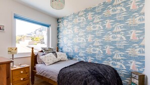 Une chambre à coucher comprenant un lit, une table de chevet en bois, une commode et une fenêtre donnant sur l’extérieur.