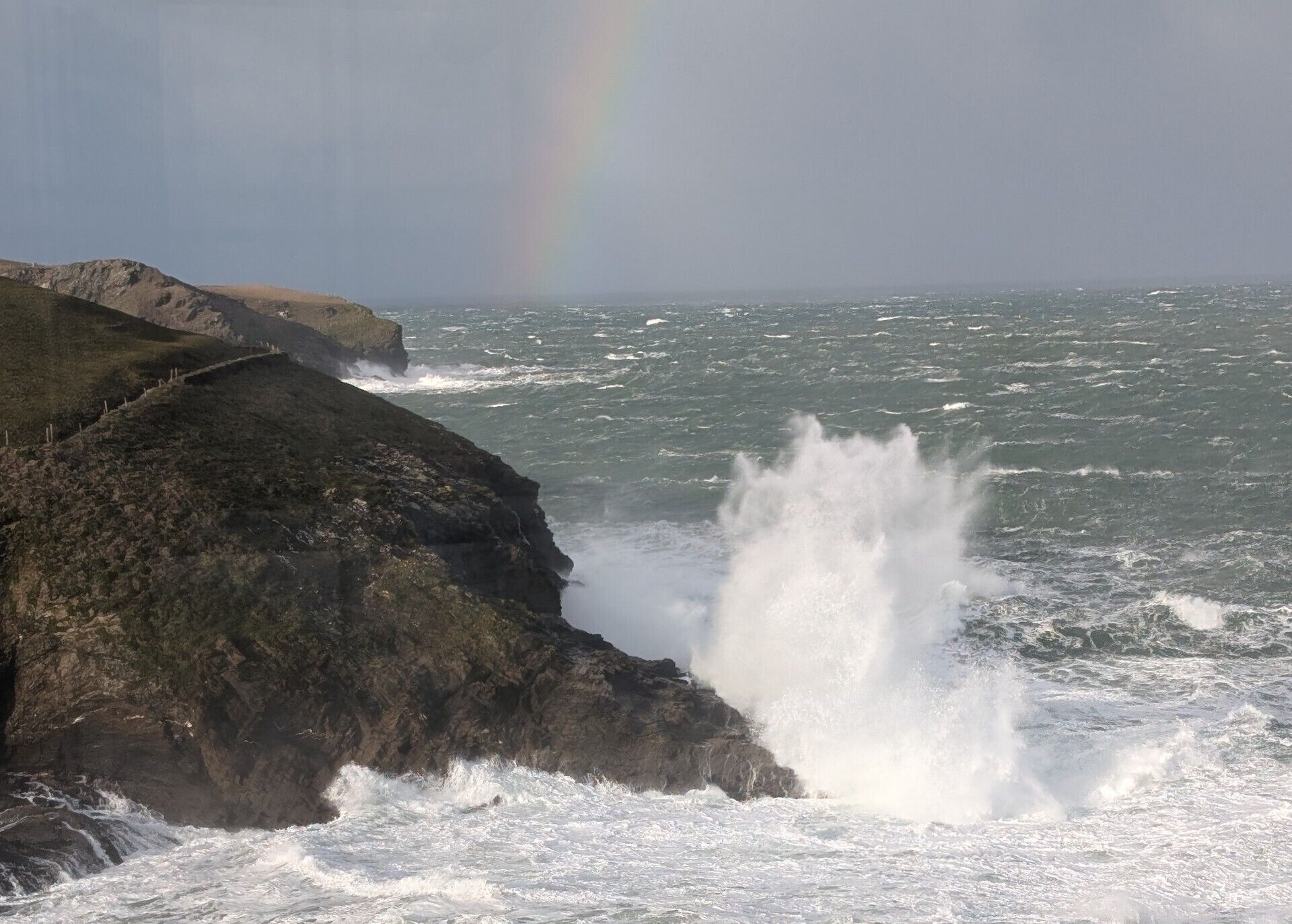 Una costa rocosa con olas rompiendo contra las rocas y un arcoíris al fondo.
